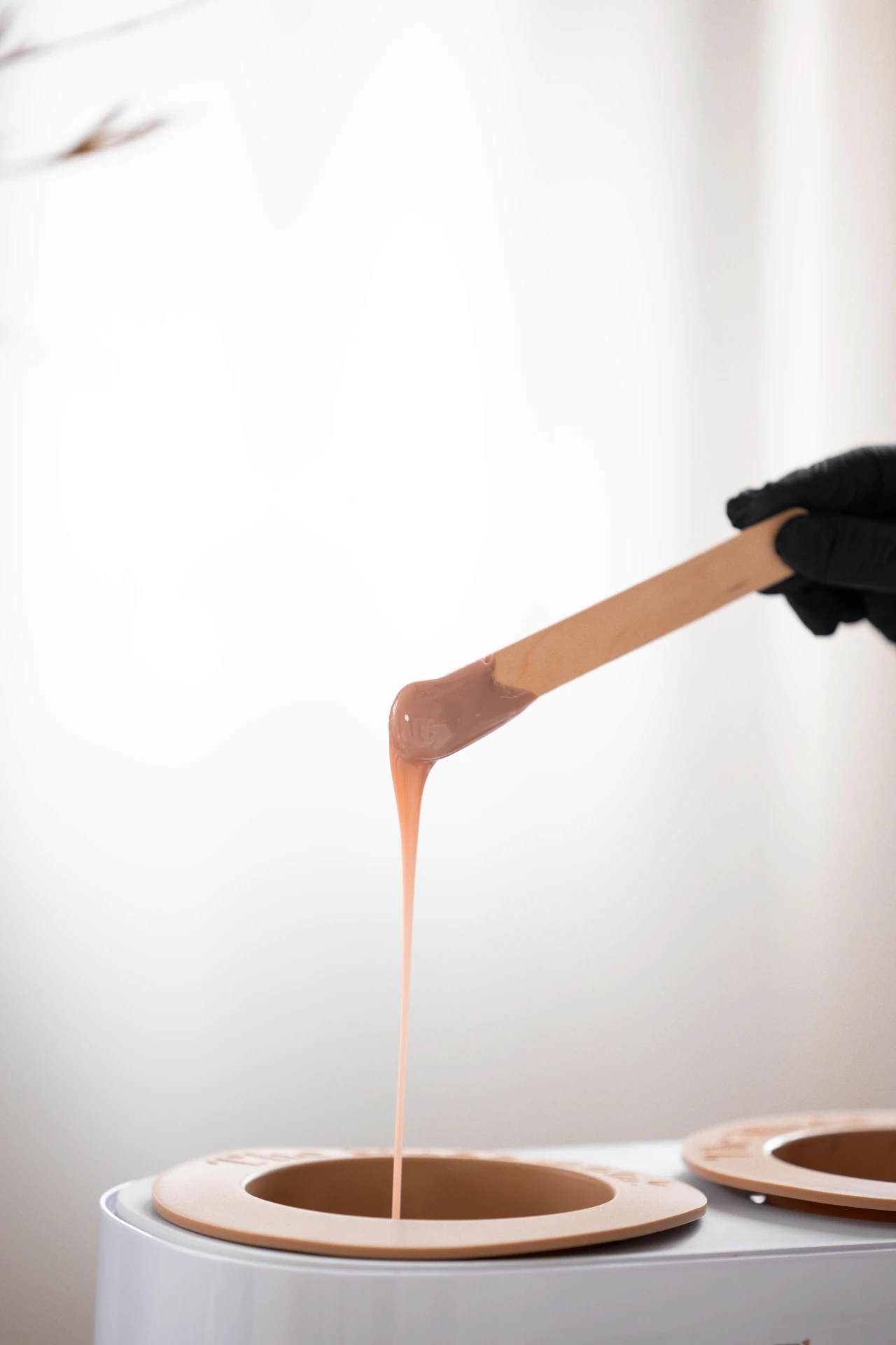 A therapist's hands holding a course certificate beside a ceramic wax pot and wooden spatula